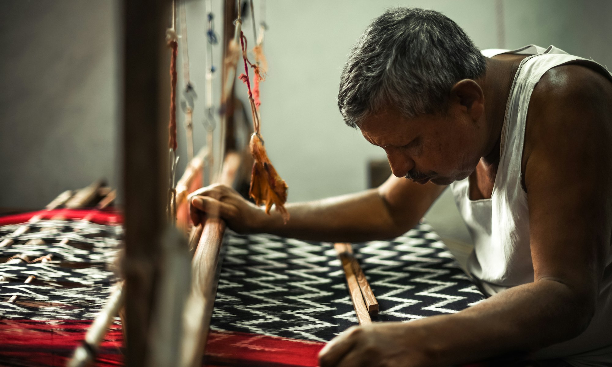 A weaver bent over an ikat loom
