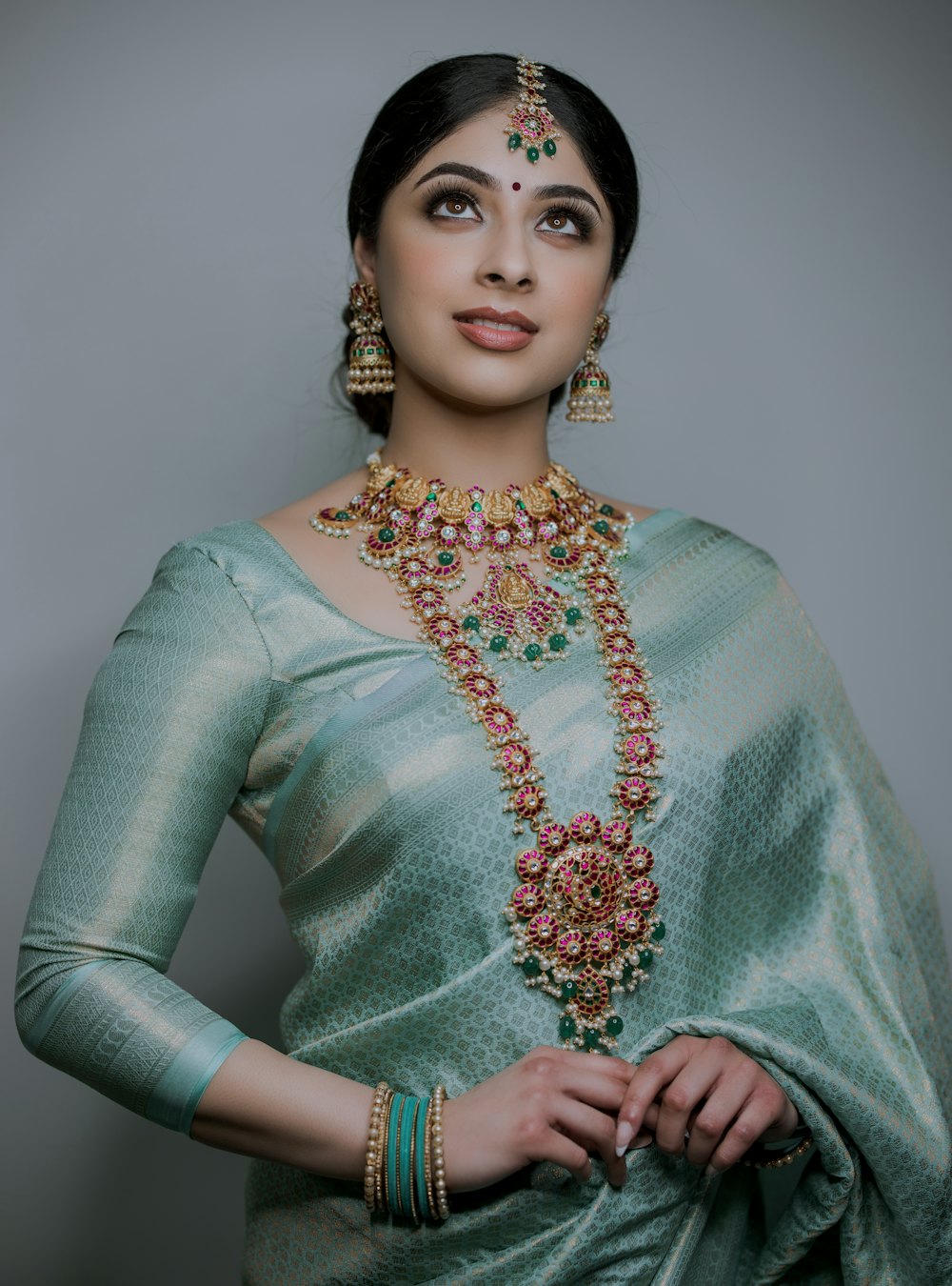 A woman in a sage green silk saree with gold temple jewellery