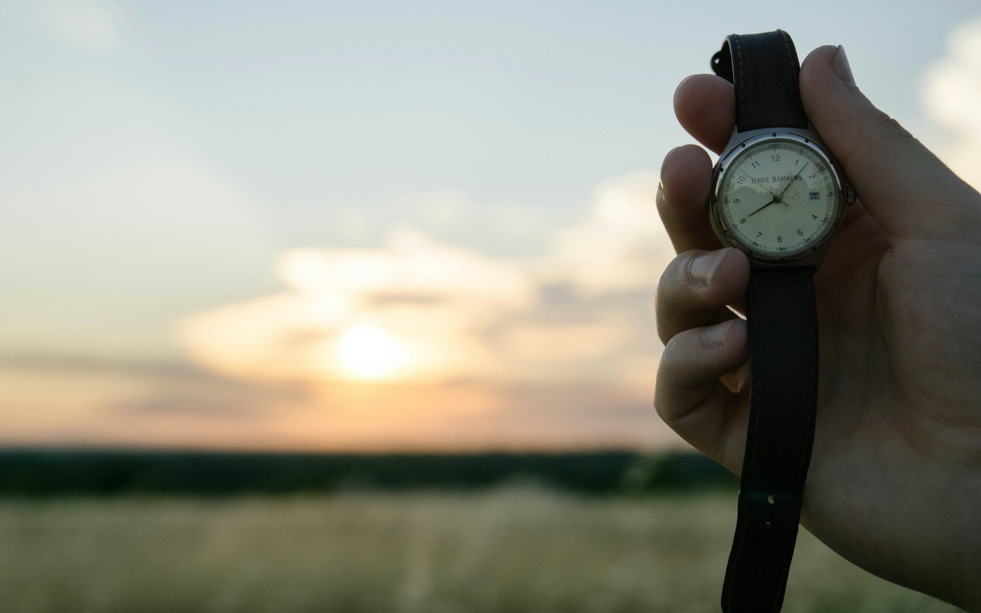 A wrist with a watch held against a setting sun