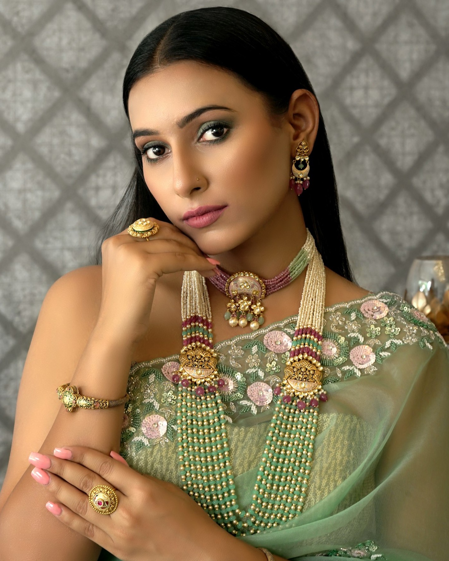 A woman wearing a layered gold and emerald necklace with matching earrings